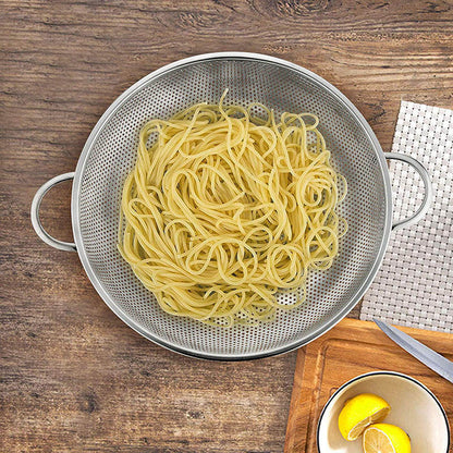 Colander with cooked spaghetti on a wooden surface with lemons and a bowl.