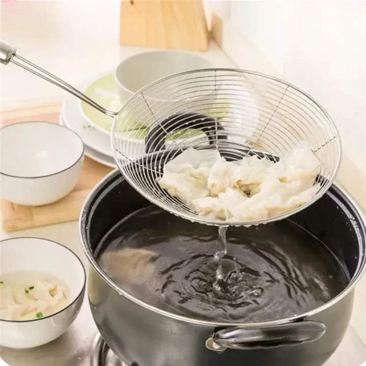 Straining cooked noodles with a metal strainer over a pot on a kitchen counter.