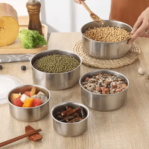 Set of stainless steel bowls containing various foods on a wooden table.