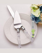 Cake server set with clear handles on a white plate, accompanied by flowers.