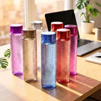 Colorful textured water bottles on a desk with a laptop and plants in the background