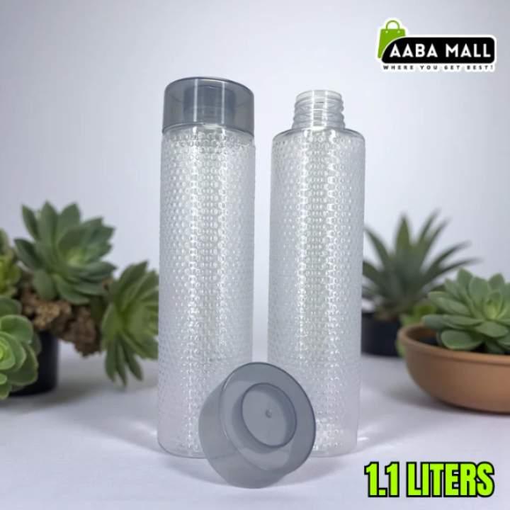 Two transparent water bottles with gray caps on a white surface with plants in the background, branded with Aaba Mall.