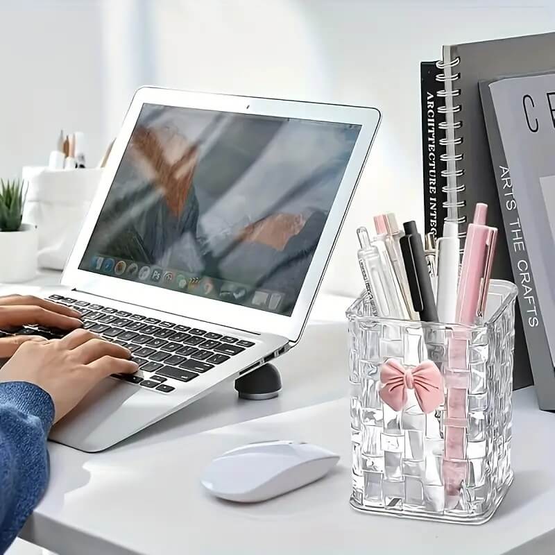 Person using a laptop with a clear pen holder on a desk