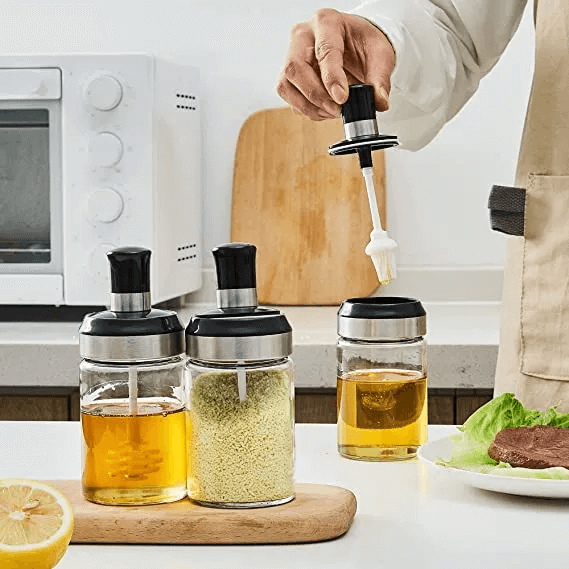 Person pouring a white liquid from a bottle into a glass container on a kitchen counter.