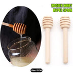 Wooden honey dipper spoon being used to pour honey into a glass jar, with two additional spoons on a white background.