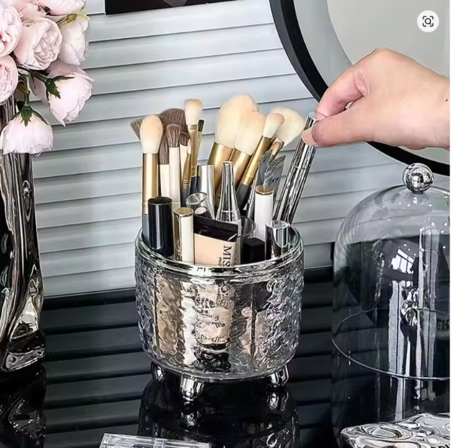 Clear acrylic rotating makeup brush holder organizer with a dustproof lid, full of cosmetic brushes on a vanity desktop