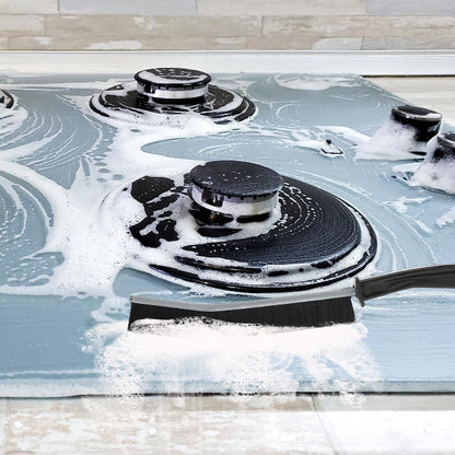 Set of two hard-bristled detail cleaning brushes with ergonomic handles, one being used to scrub white bathroom tile grout to show effectiveness.