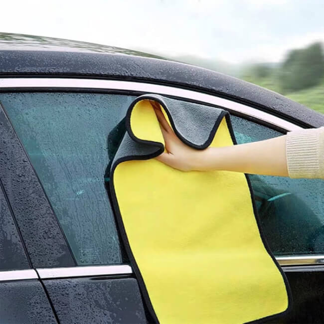 Person cleaning a car window with a yellow microfiber cloth