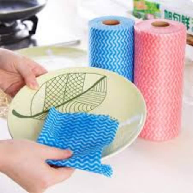 Cleaning cloth with a leaf design held by a hand, with two rolls of paper towels in the background.