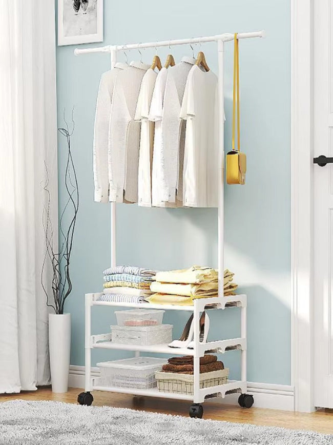 Full view of white adjustable metal clothes rack with 3 wire shelves, holding hanging clothes, shoes, and folded towels in a modern bedroom setting.