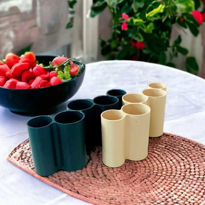 Set of green and beige planters on a table with a bowl of fruits in the background.