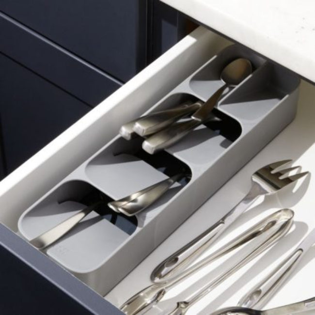 Multi-layer kitchen drawer cutlery organizer tray in grey, shown with spoons, forks, and knives stored vertically in the tiered, overlapping compartments for maximum space saving.