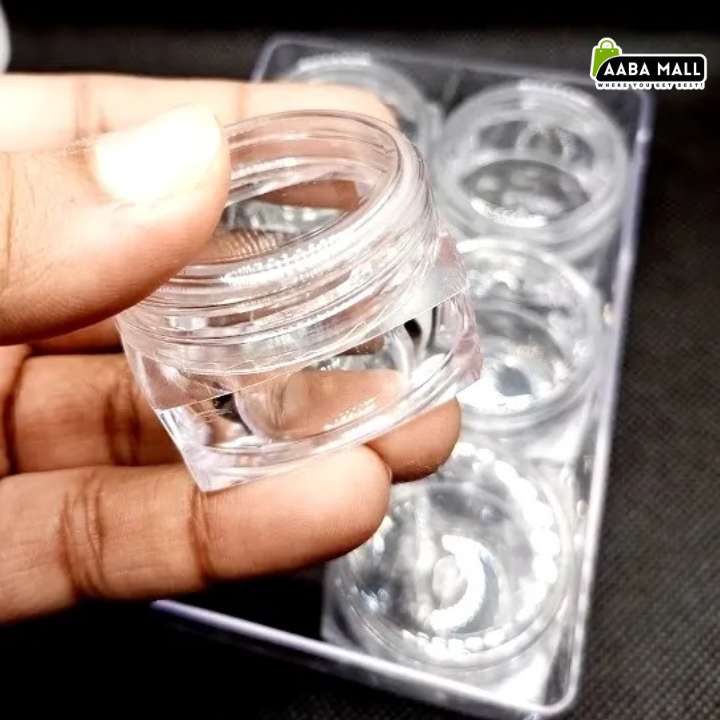 A hand holding a small clear plastic cosmetic jar in front of a blister pack containing multiple matching empty jars. The AABA MALL logo is visible in the top right corner.