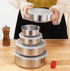 Set of stainless steel bowls with lids on a wooden table, person holding one bowl.