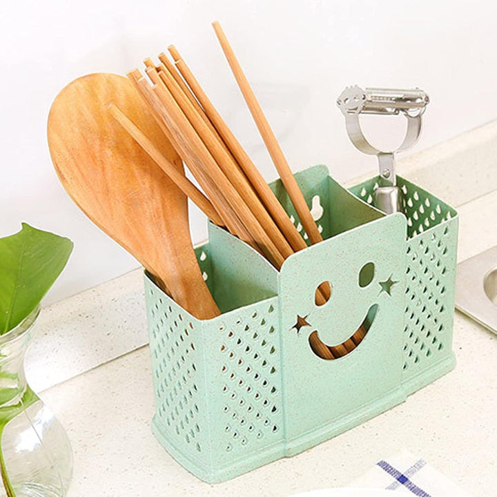 A green plastic cutlery holder with a smiley face design, containing various wooden utensils such as spoons and chopsticks.