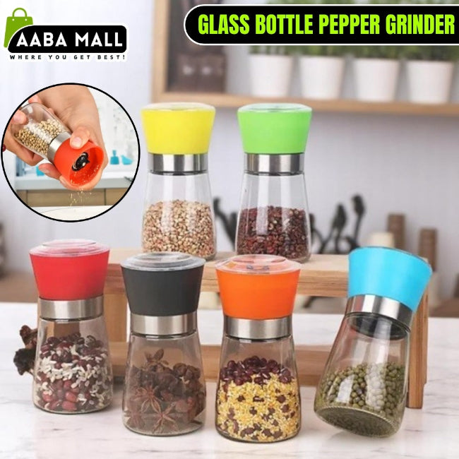 Elegant stainless steel pepper grinder with a clear glass body, shown set to a coarse grind, being used to season a dish of fresh food on a wooden counter.