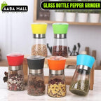 Elegant stainless steel pepper grinder with a clear glass body, shown set to a coarse grind, being used to season a dish of fresh food on a wooden counter.