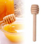 Close-up of a single 8 cm wooden honey dipper stick with a spiral grooved head, shown drizzling golden honey over a slice of toast.