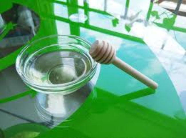 Close-up of a single 8 cm wooden honey dipper stick with a spiral grooved head, shown drizzling golden honey over a slice of toast.