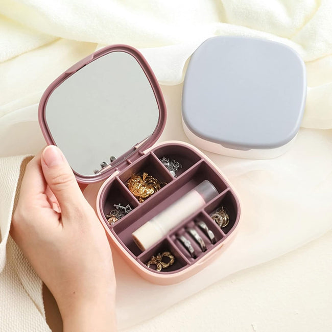 Closed view of a portable jewelry organizer travel box in blush pink, with the lid open showing velvet interior compartments and a built-in mirror.
