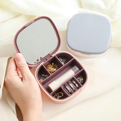 Closed view of a portable jewelry organizer travel box in blush pink, with the lid open showing velvet interior compartments and a built-in mirror.