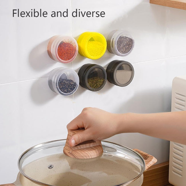 Set of three silver magnetic spice tins with clear transparent lids, shown attached vertically to the side of a stainless steel refrigerator, filled with different colored spices.