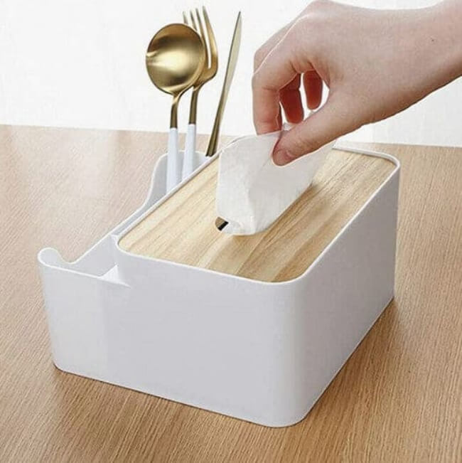 White and wooden tissue holder with utensils on a light wood surface