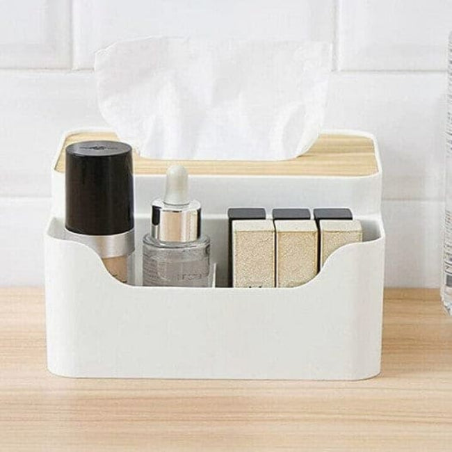 Wooden desktop organizer box with a flat top, showing a tissue box compartment on one side and three partitioned slots filled with remotes and pens on the other side.