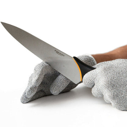 Close-up of a hand wearing a grey Level 5 cut resistant safety glove, securely holding a large onion while the other hand uses a sharp chef's knife for slicing on a cutting board.