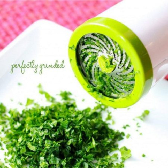 Handheld stainless steel herb mill grinder and spice chopper, shown with dry oregano inside, illustrating the sharp internal cutting mechanism and brushed steel finish.