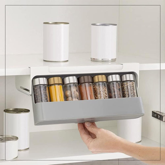 White plastic under shelf spice rack organizer, shown adhered beneath a kitchen cabinet shelf, neatly holding several rows of small spice jars with clear labels.
