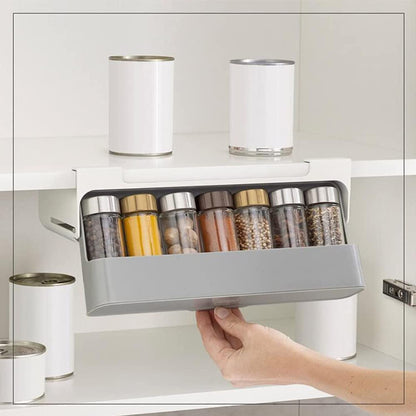 White plastic under shelf spice rack organizer, shown adhered beneath a kitchen cabinet shelf, neatly holding several rows of small spice jars with clear labels.