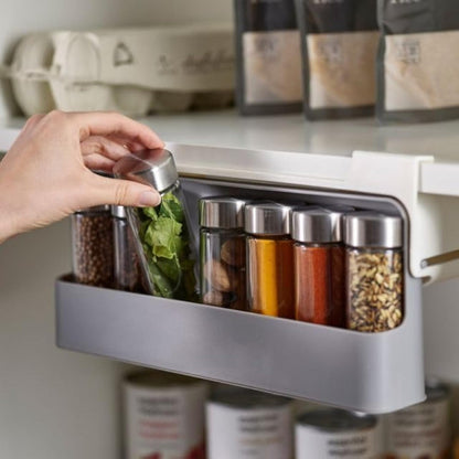 White plastic under shelf spice rack organizer, shown adhered beneath a kitchen cabinet shelf, neatly holding several rows of small spice jars with clear labels.