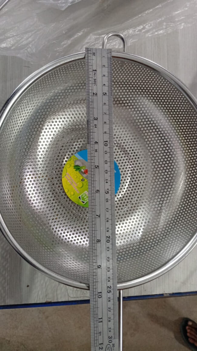 Metallic colander with a ruler for scale on a plain background